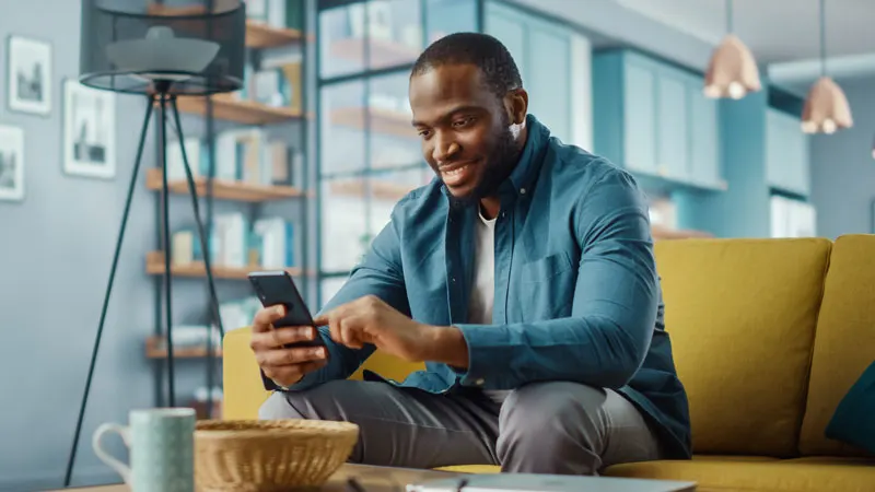 man sitting on couch, looking at phone and smiling